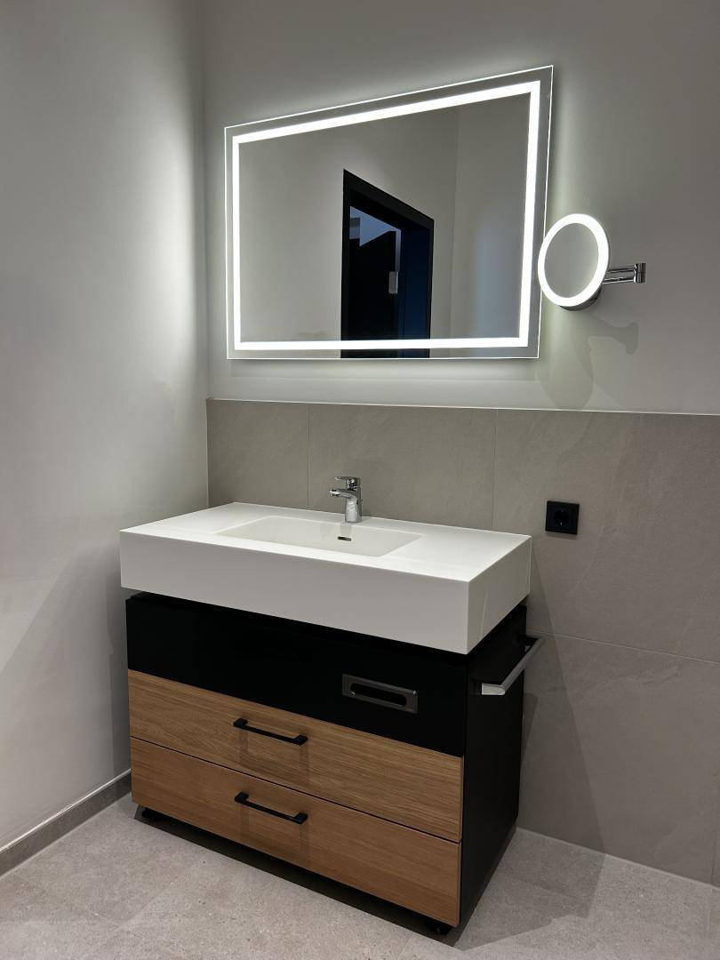 Modernes Badezimmer mit beleuchtetem Spiegel, Einzelwaschbecken und Holzunterschrank.