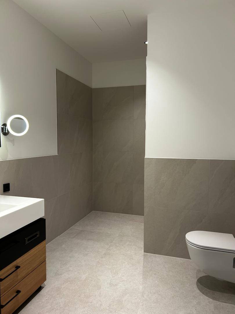Geräumiges Badezimmer mit begehbarer Dusche, Wand-WC und modernen Fliesen.