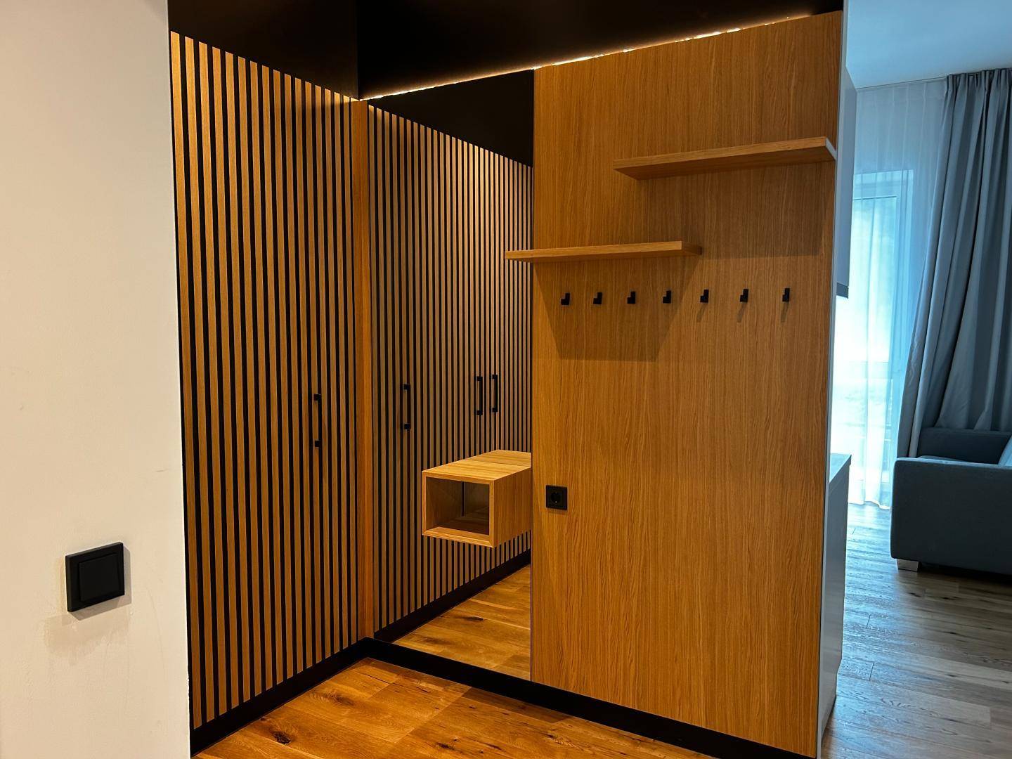 Moderner Eingangsbereich mit Holzlamellenwand, Spiegel und Garderobenhaken.