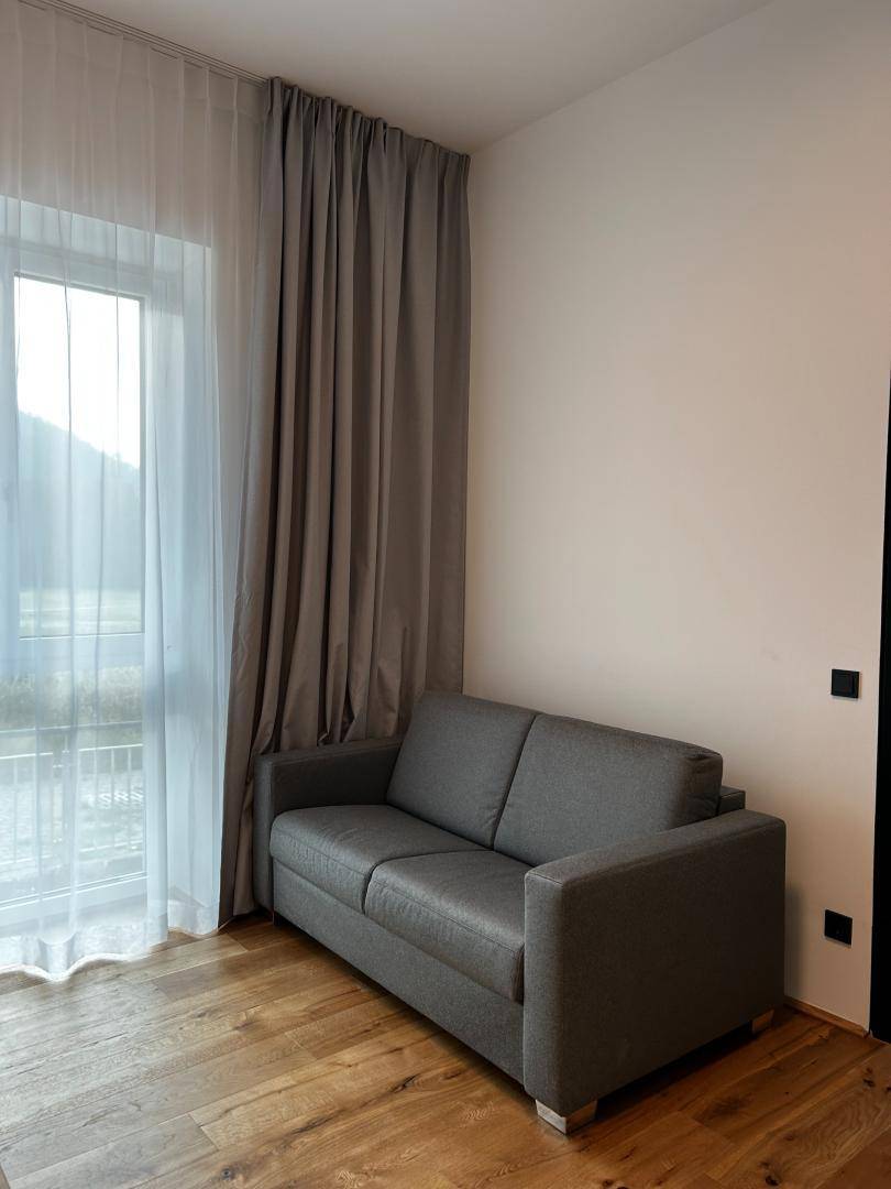 Helles Wohnzimmer mit bequemer Couch, Holzboden und großem Fenster mit Vorhängen.