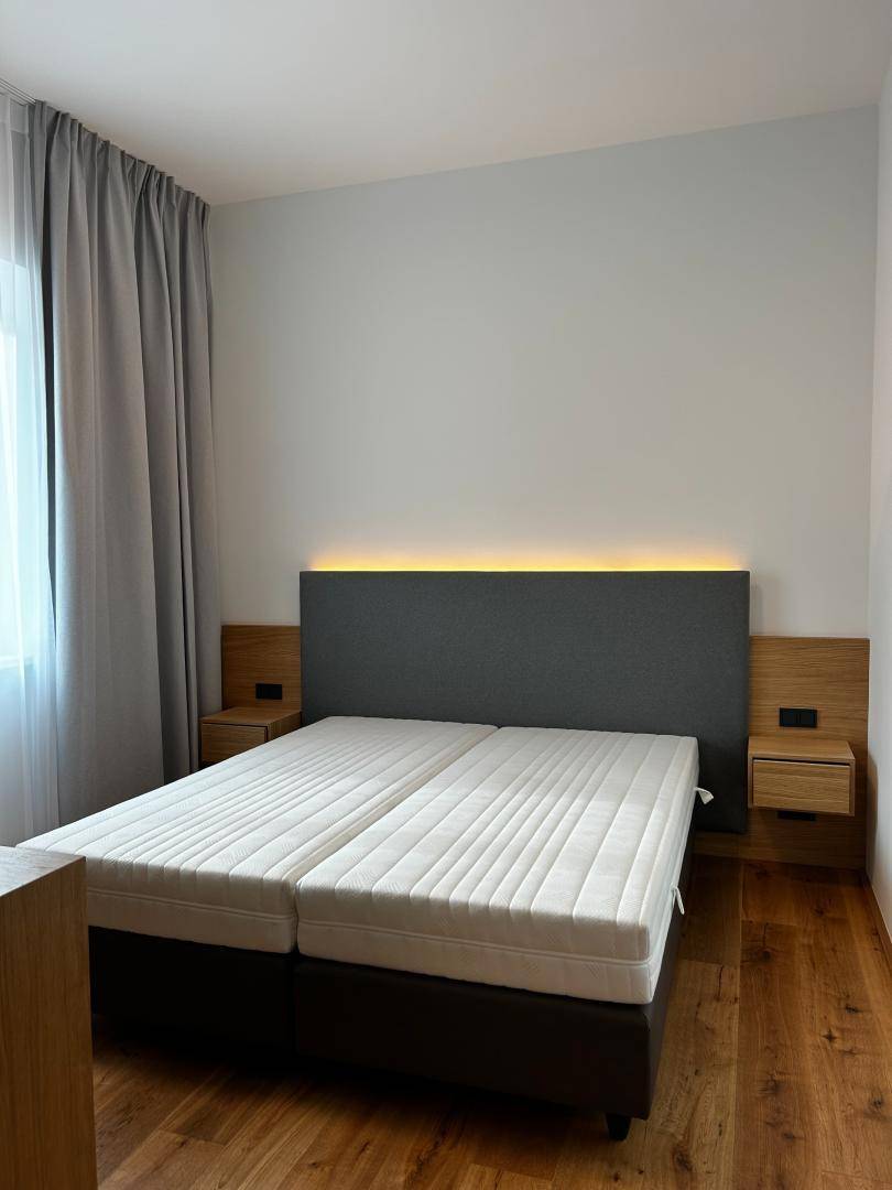 Schlafzimmer mit Doppelbett, Holzboden und indirekter Beleuchtung am Kopfteil.
