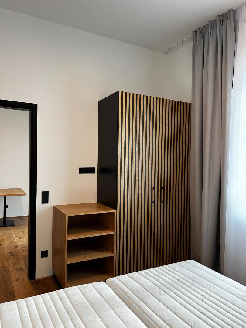 Schlafzimmer mit Kleiderschrank, offenem Regal und Holzboden neben dem Bett.