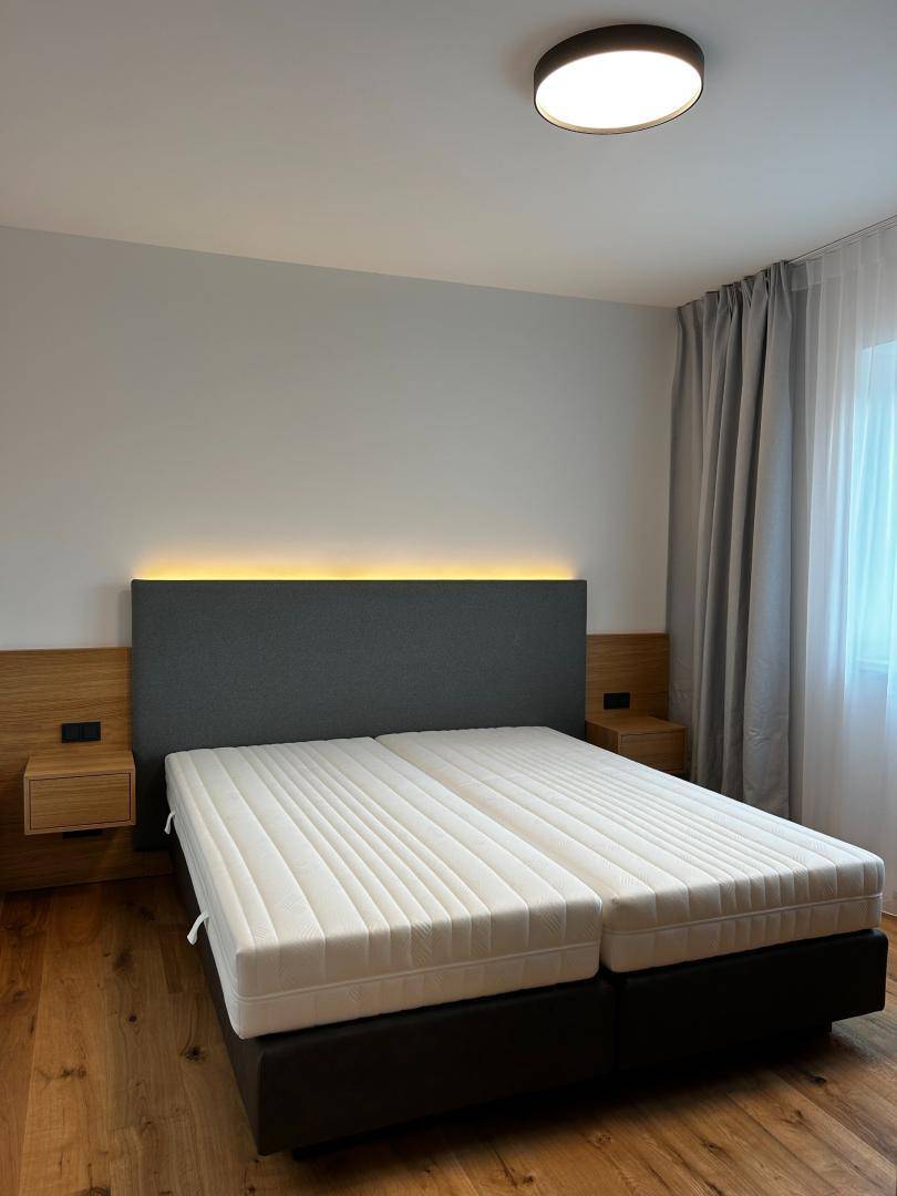Schlafzimmer mit Doppelbett, Holzboden und indirekter Beleuchtung am Kopfteil für eine gemütliche Atmosphäre.