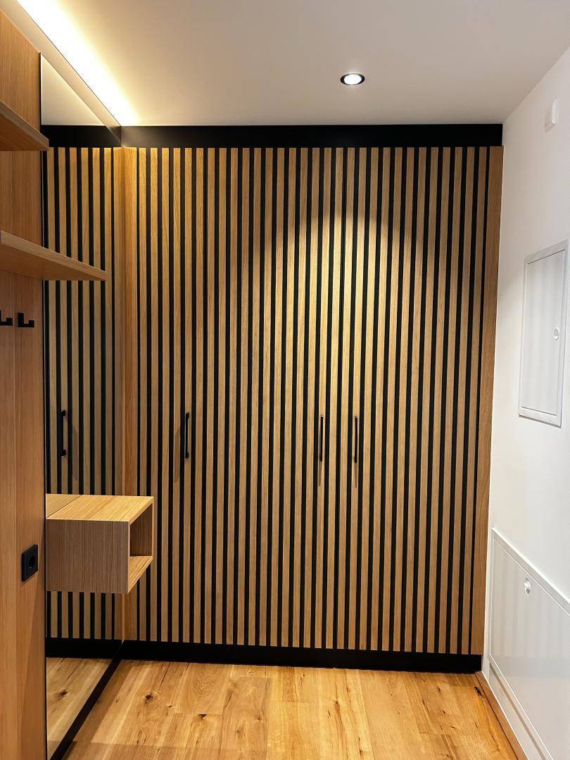 Moderner Einbauschrank mit Holzlamellen und integrierter Beleuchtung im Flurbereich, sehr stilvoll.
