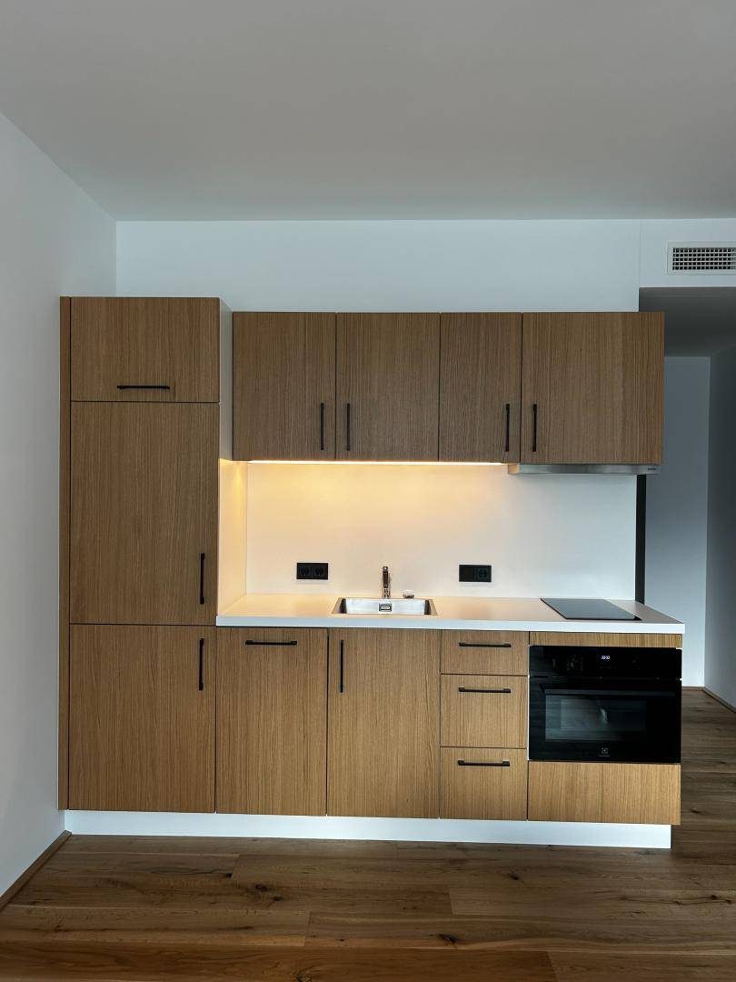 Moderne Küchenzeile mit Holzfronten, integrierten Geräten und heller Arbeitsplatte in neuwertigem Zustand.