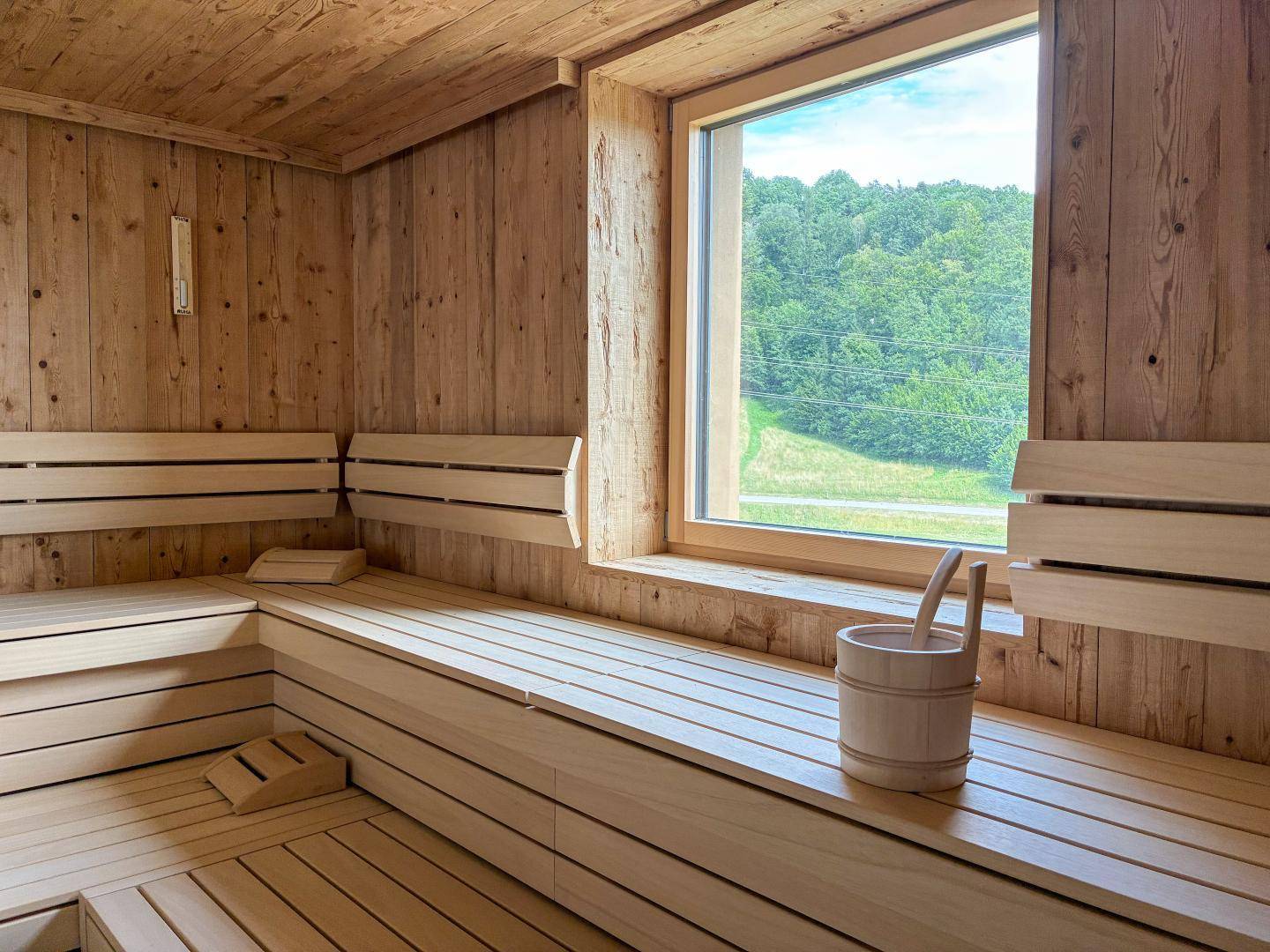 Helle Sauna mit Holzverkleidung, Sitzbänken und einem großen Fenster mit Blick ins Grüne.
