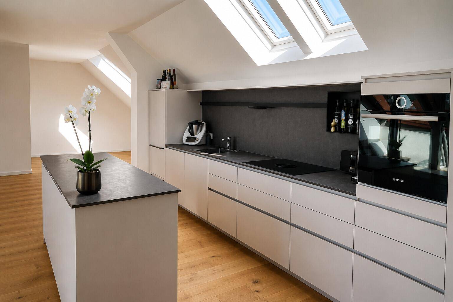 Moderne Einbauküche mit Kochinsel, hochwertigen Geräten und Dachfenstern für helles Ambiente.