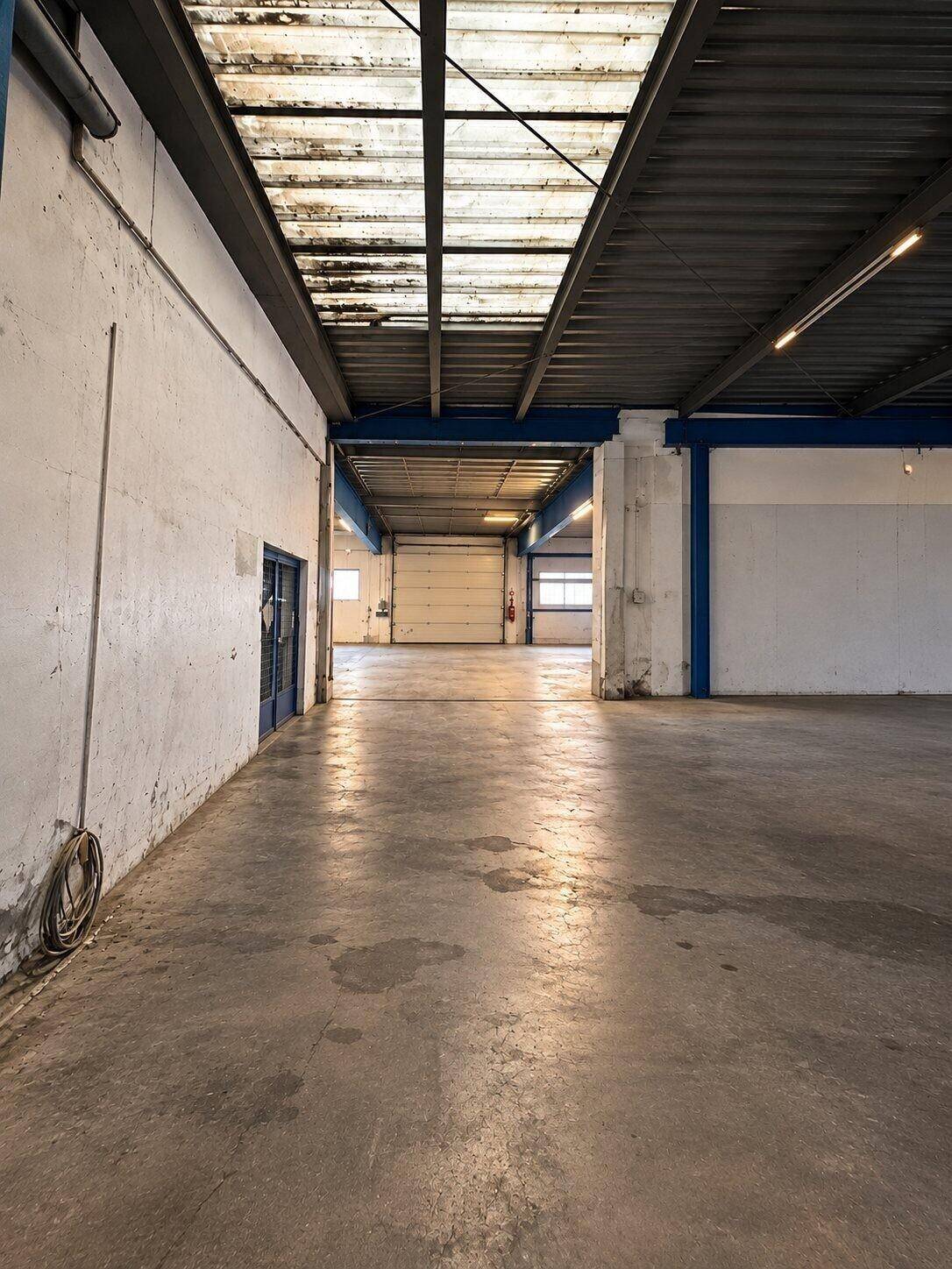Langer Gang in der Lagerhalle mit Betonboden, blauen Trägern und Oberlichtern für Tageslichteinfall.
