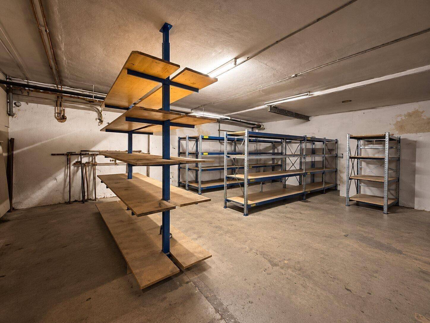 Kellerraum mit verschiedenen Regalsystemen, Betonboden und sichtbaren Installationen an der Decke.