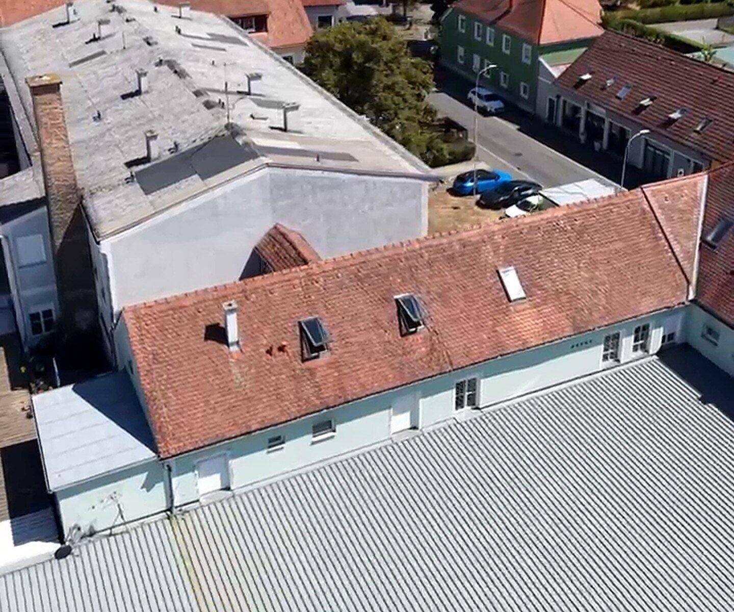 Luftaufnahme eines Gebäudekomplexes mit roten Ziegeldächern, Flachdach und umliegender Bebauung.