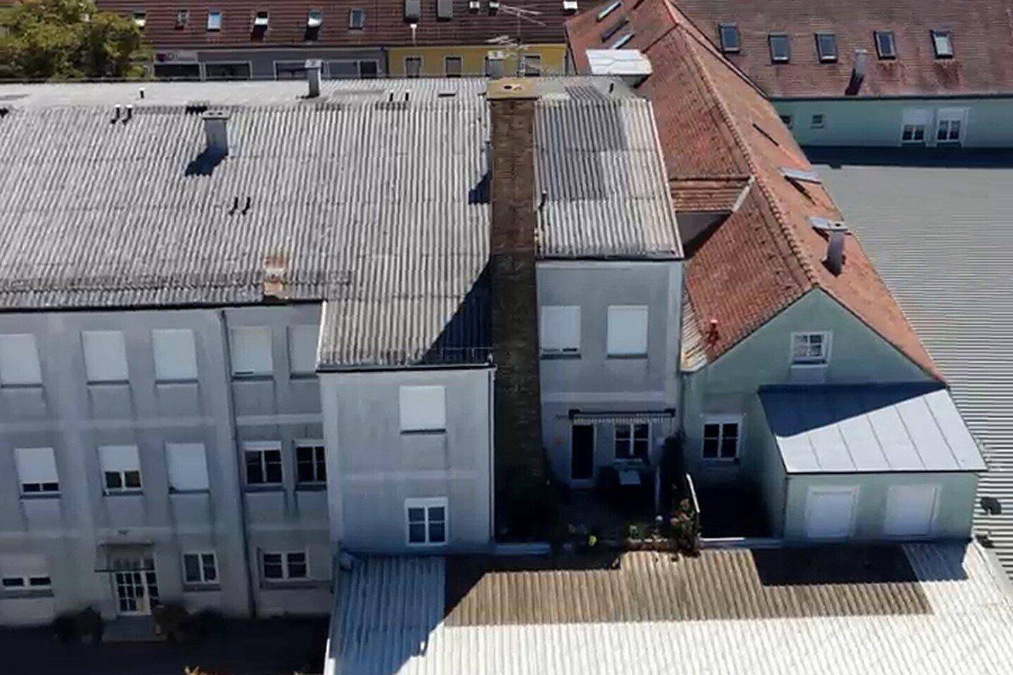 Luftaufnahme eines mehrstöckigen Gebäudes mit Schornstein, Rollläden und angrenzenden Dächern.