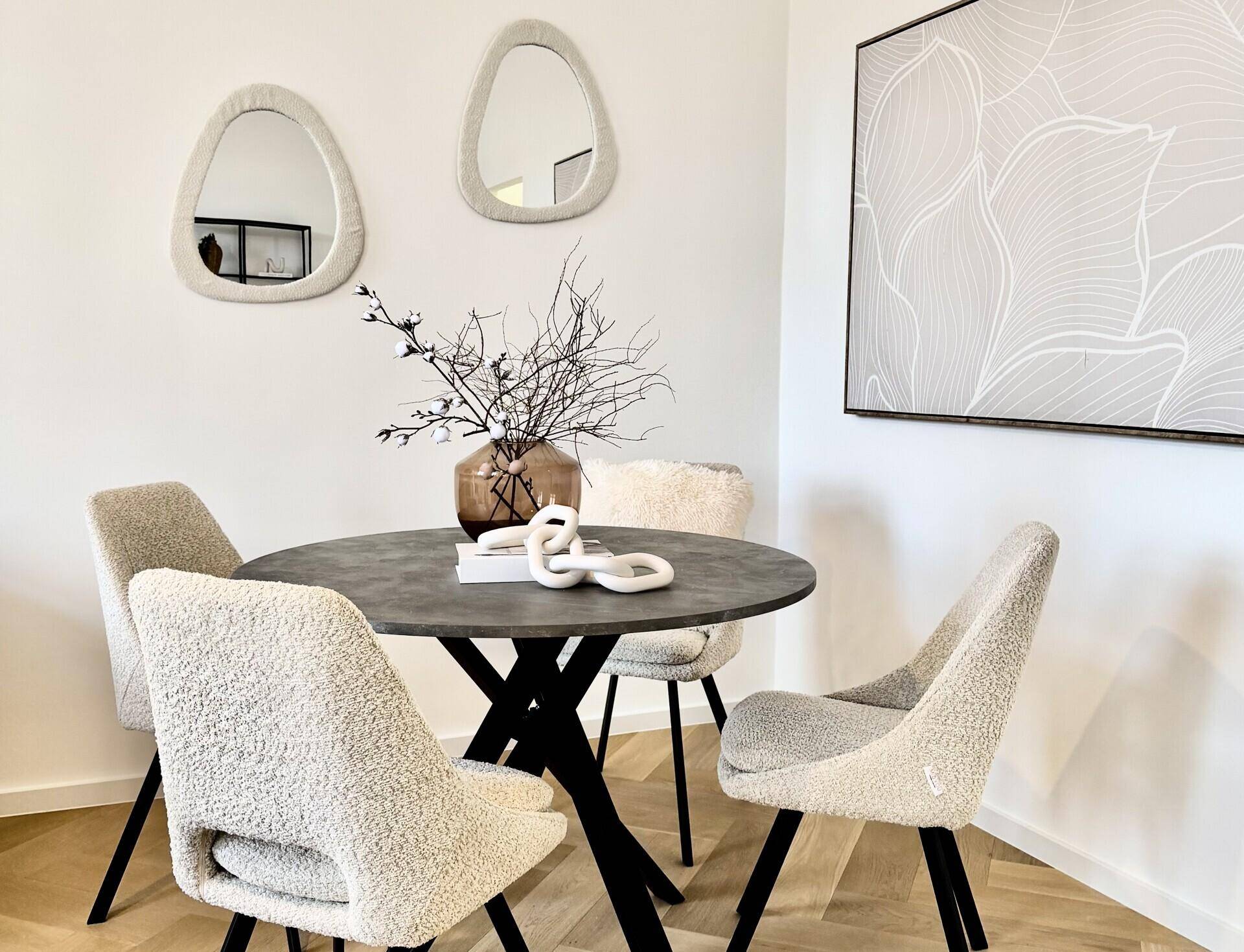 Moderner Essbereich mit rundem Tisch, bequemen Stühlen und dekorativen Spiegeln an der Wand.