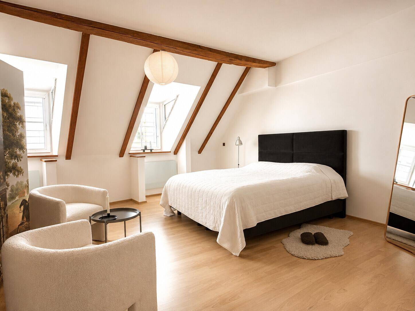 Schlafzimmer im Dachgeschoss mit Holzbalken, Dachfenstern und modernem Bett.