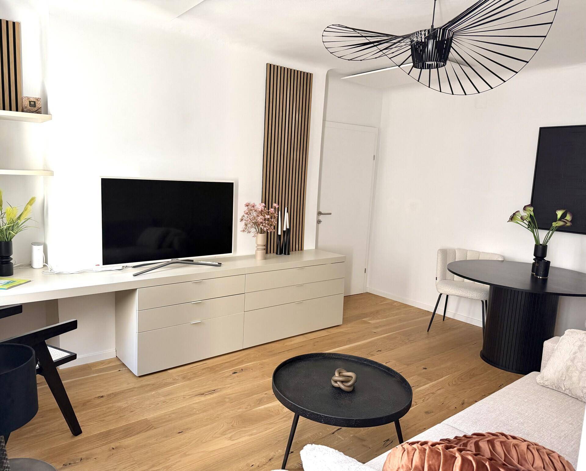 Offener Wohn- und Essbereich mit Holzboden, modernem TV-Möbel und Designerleuchte.