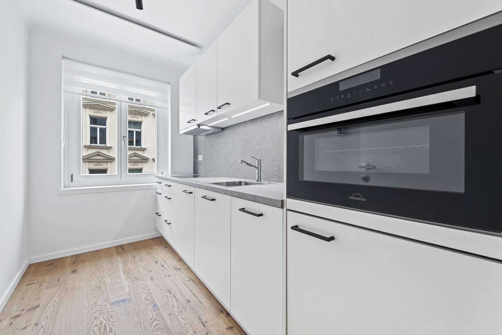 Moderne weiße Küche mit integriertem Backofen und Mikrowelle sowie Blick auf die Straße.