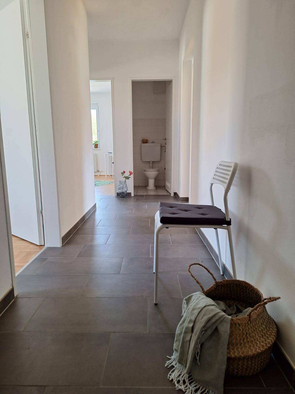 Heller Flur mit dunklen Fliesen, der zu einem separaten WC führt.