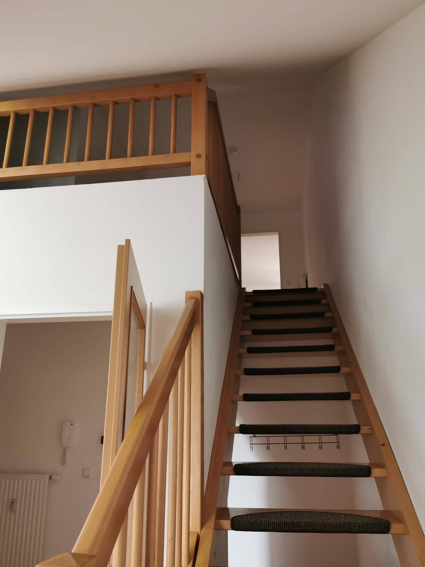 Holztreppe mit Geländer führt zu einem oberen Bereich oder einer Galerie, typisch für Maisonette-Wohnungen.
