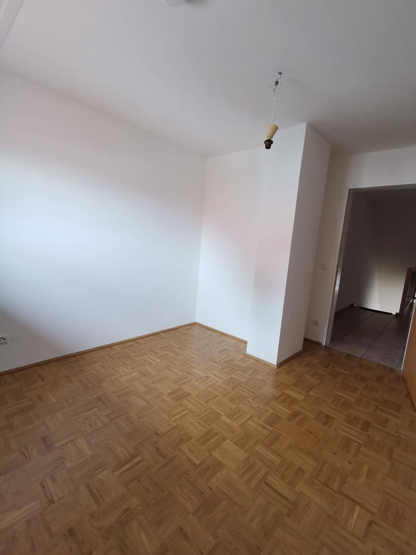 Leerer Raum mit hellem Parkettboden und weißen Wänden, bereit zur individuellen Gestaltung.