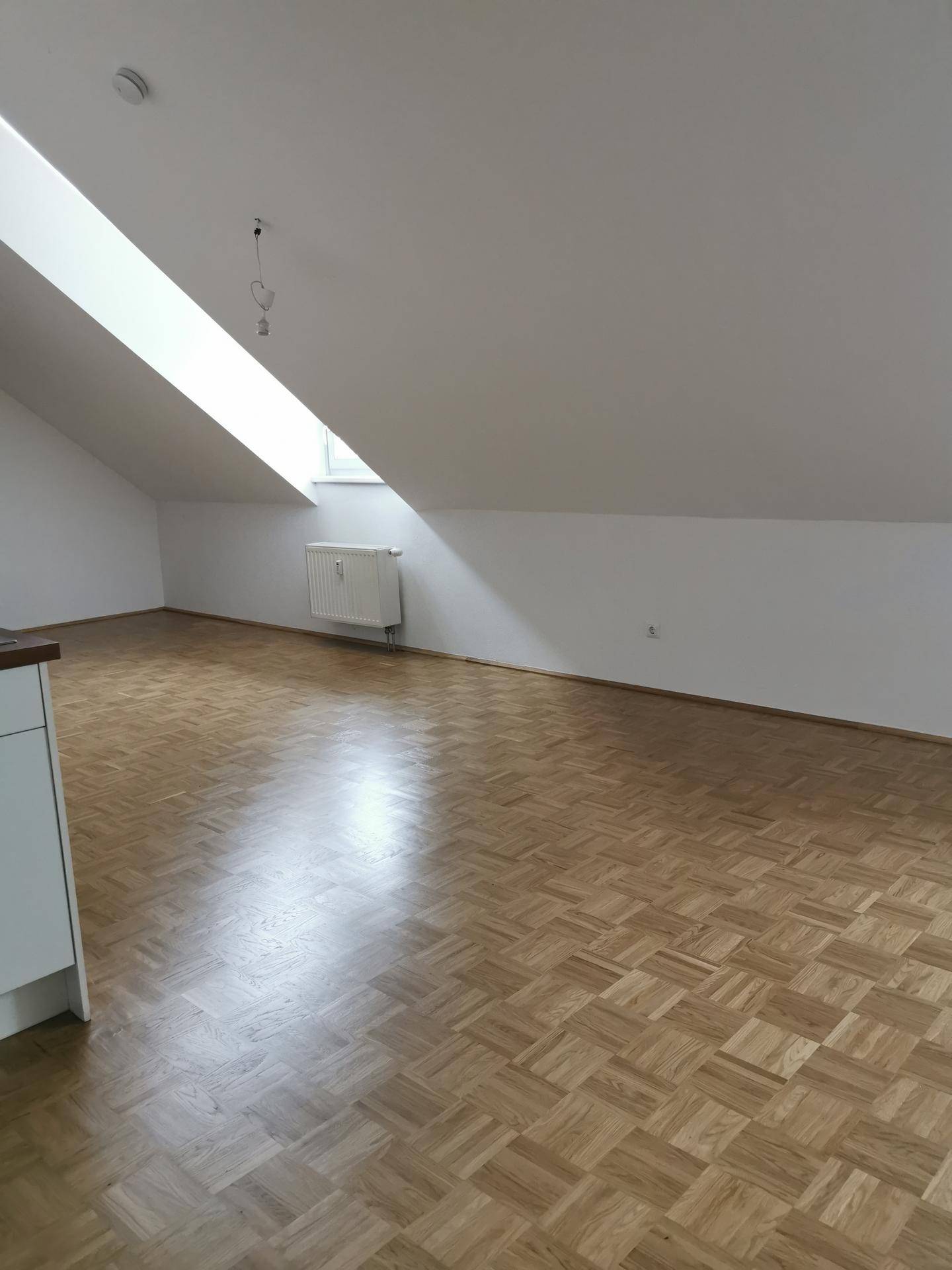 Heller Dachgeschossraum mit Parkettboden, Dachschräge und einem Dachfenster, ideal als Wohnbereich.