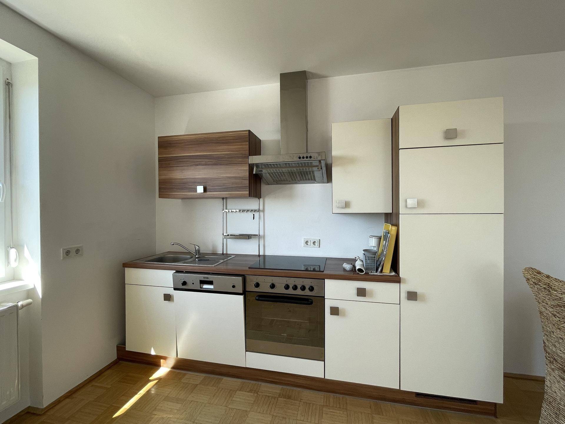 Helle Küche mit Einbaugeräten, Parkettboden und Fenster für Tageslicht.