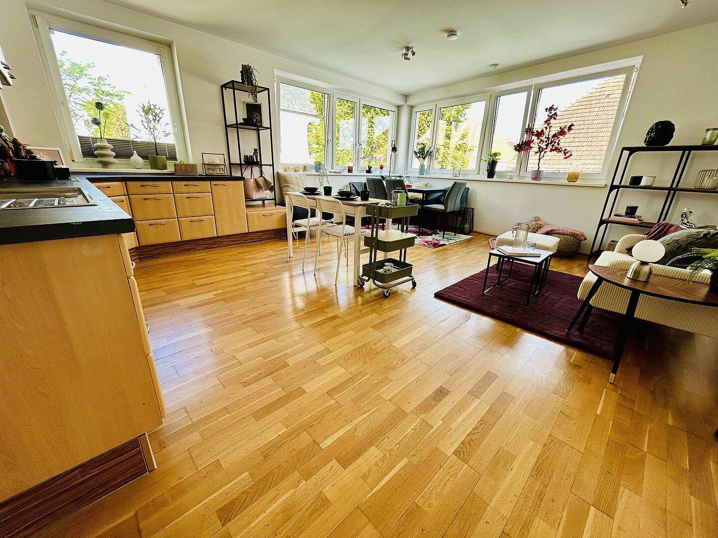 Offener Wohn-Essbereich mit integrierter Küche, Holzboden und großen Fenstern für viel Licht.