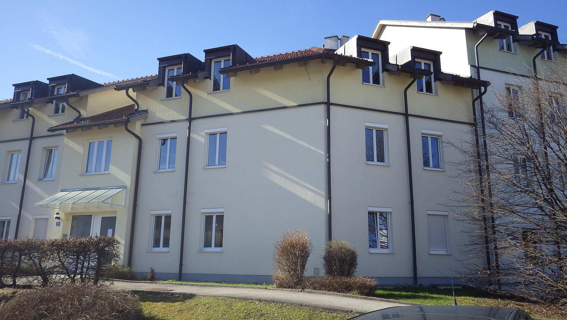 Wohngebäude mit heller Fassade und Mansarddach an einem sonnigen Tag.