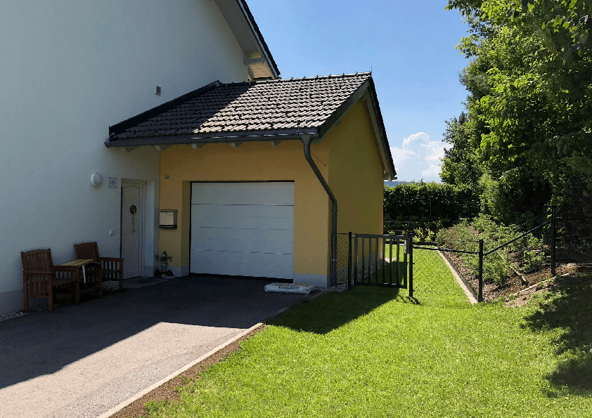 Garage mit Einfahrt und angrenzendem gepflegten Gartenbereich unter strahlend blauem Himmel.