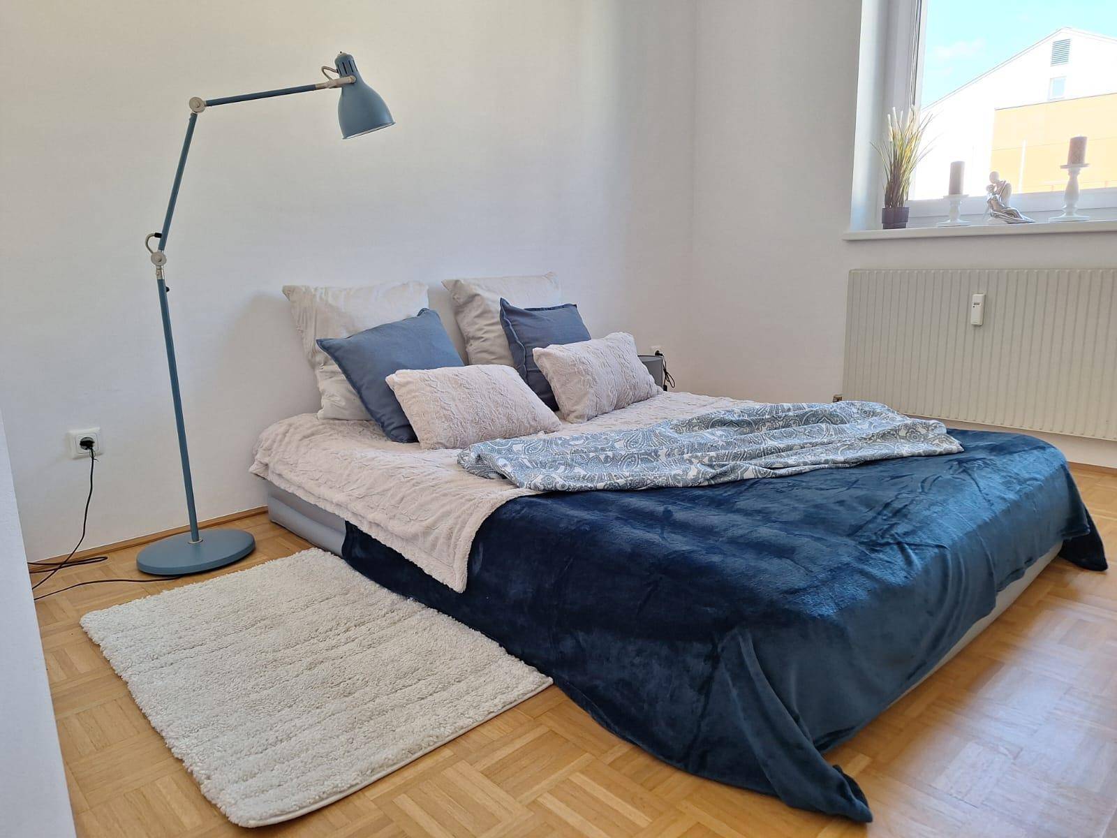 Schlafzimmer mit Holzboden, einem großen Bett und einer modernen Stehlampe.
