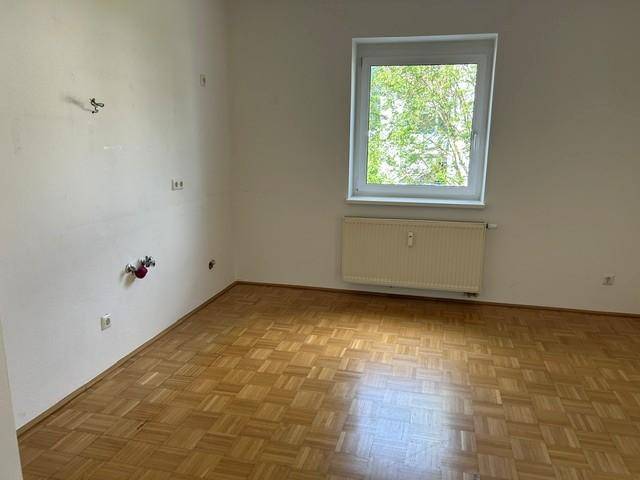 Leerer Raum mit klassischem Parkettboden, Fenster und Heizkörper.