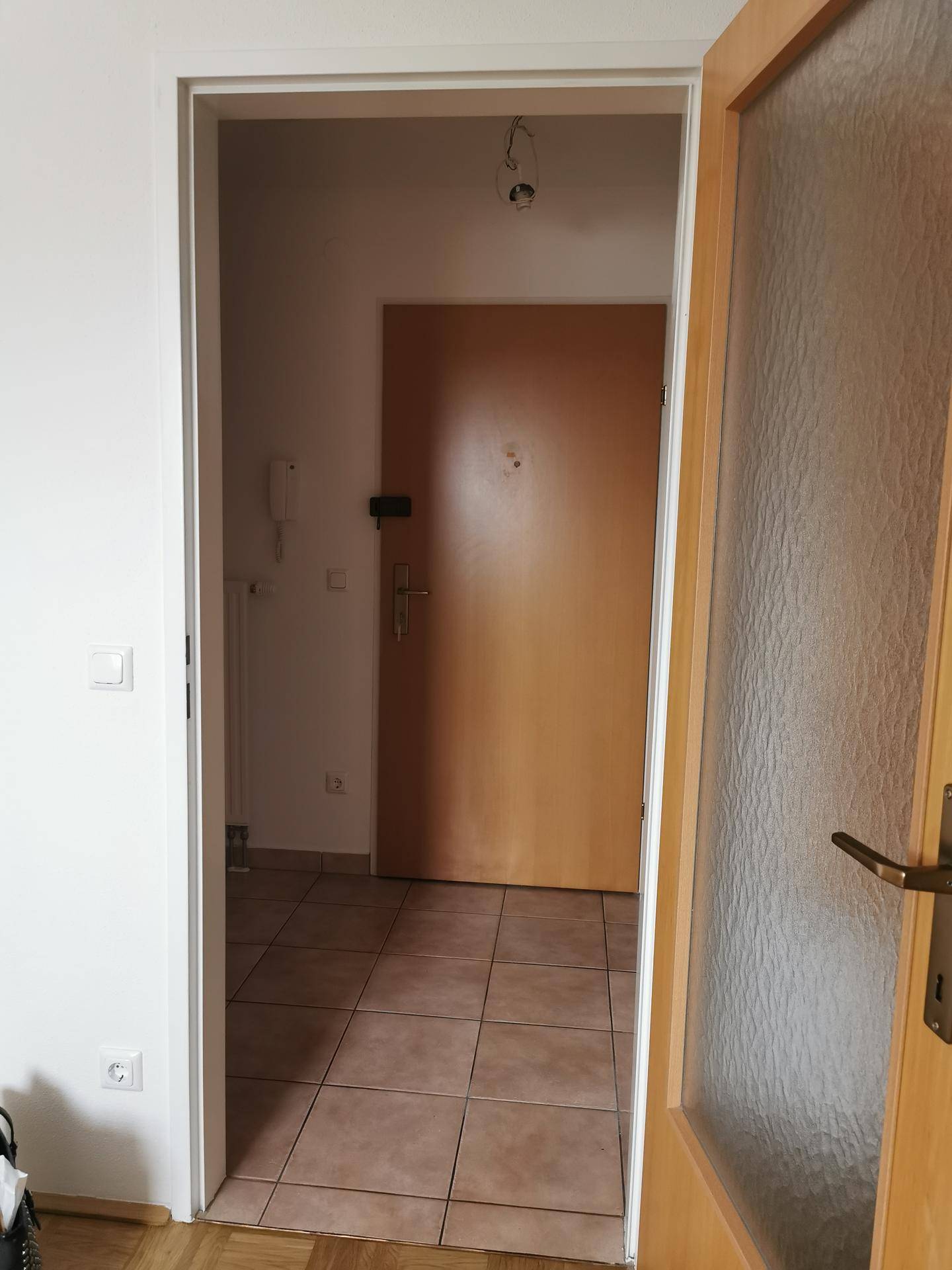 Blick durch eine offene Tür in einen Flur mit Fliesenboden und einer Holzeingangstür.