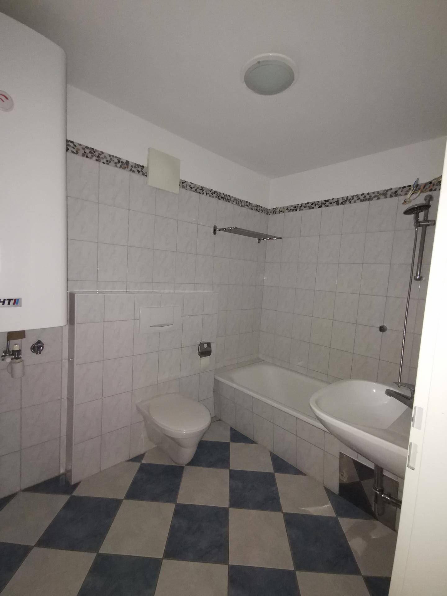 Badezimmer mit karierten Fliesen, Badewanne, Toilette und Waschbecken, ausgestattet mit einem Warmwasserboiler.