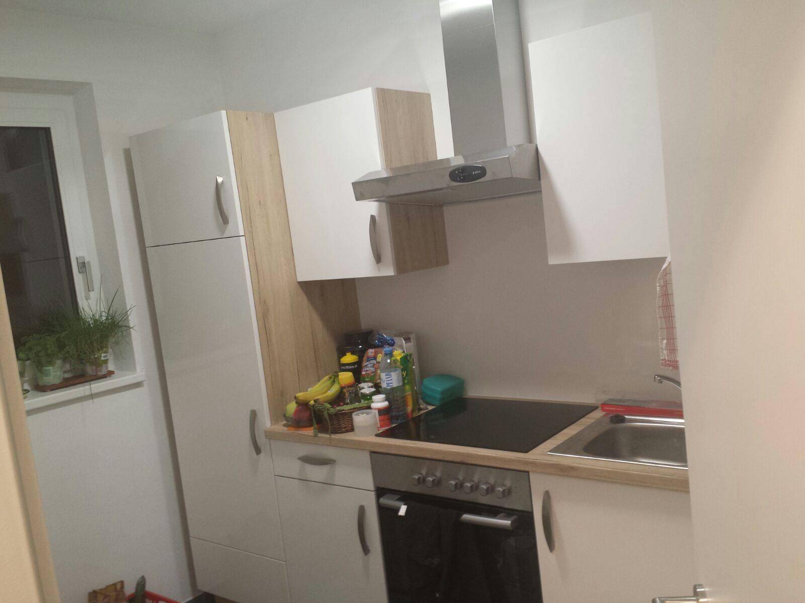 Kleine, funktionale Küche mit weißen und holzfarbenen Schränken, Herd und Dunstabzugshaube.