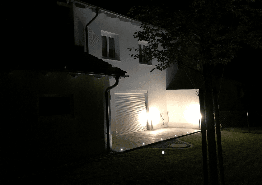 Beleuchtete Holzterrasse und Gartenbereich am Abend mit stimmungsvoller Außenbeleuchtung des Hauses.