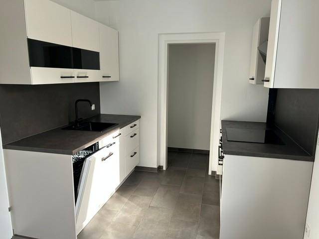 Moderne Küche mit weißen Schränken, dunklen Arbeitsplatten und Fliesenboden.