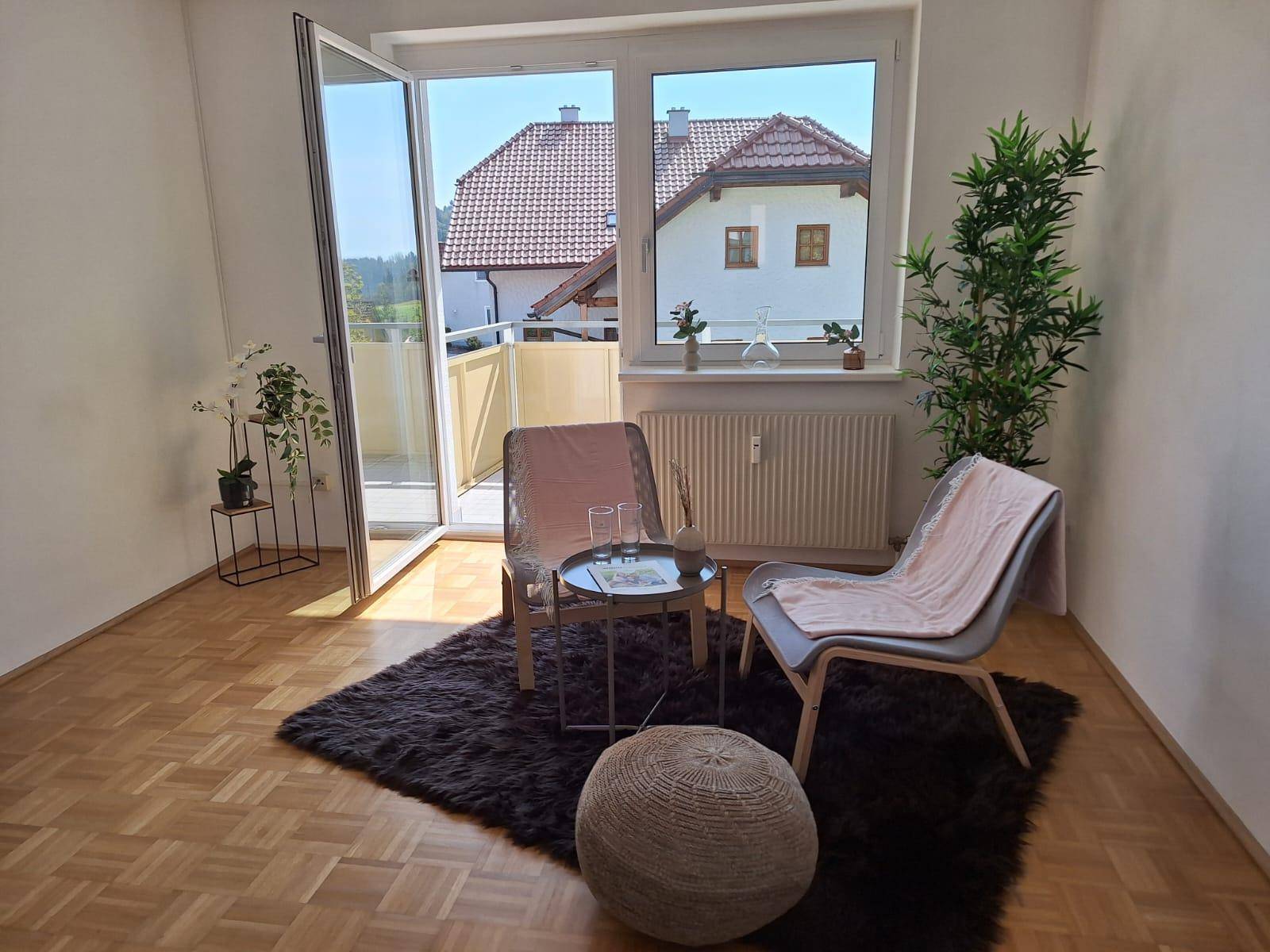 Helles Wohnzimmer mit Parkettboden, zwei Sesseln und Zugang zu einem Balkon.