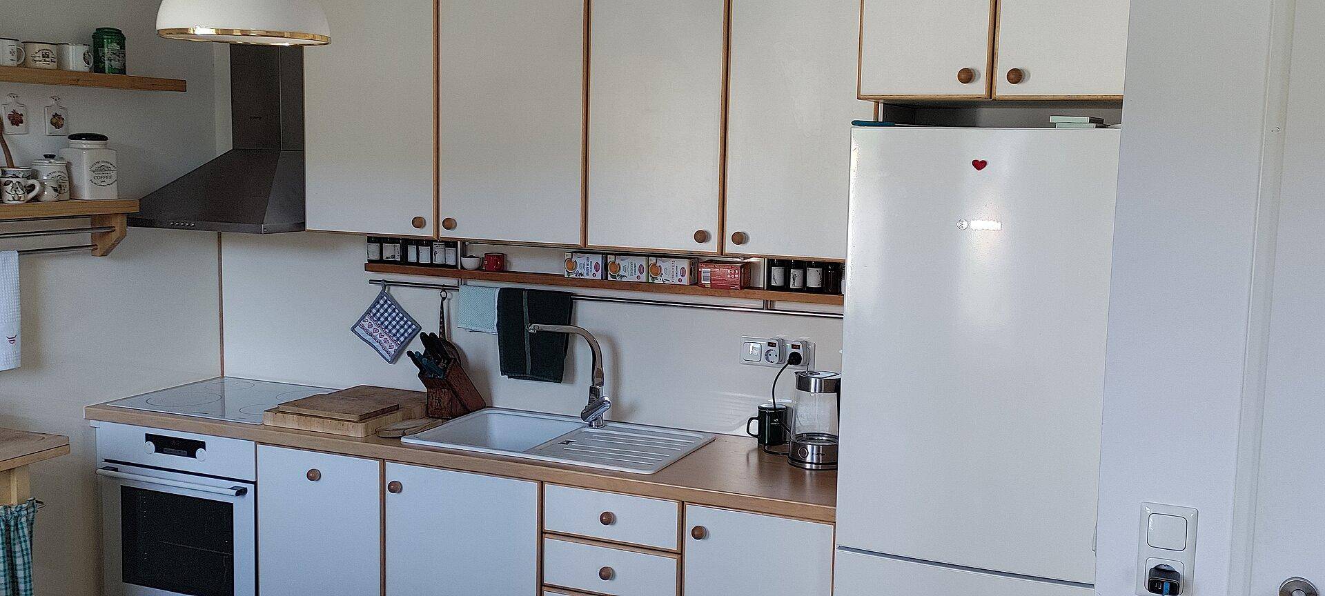 Helle, funktionale Küche mit weißen Schränken, Holzdetails, integriertem Backofen und Kühlschrank.