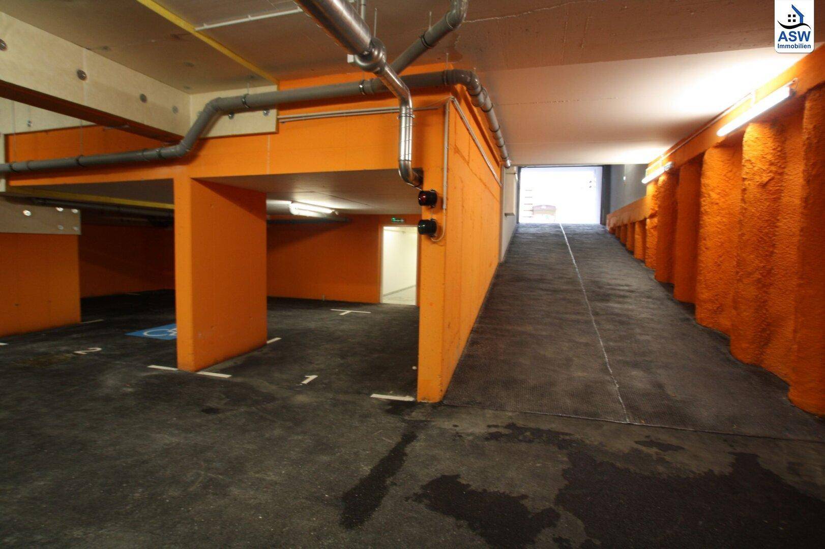 Tiefgarage mit orangefarbenen Wänden, Zufahrtsrampe und sichtbaren Installationen an der Decke.