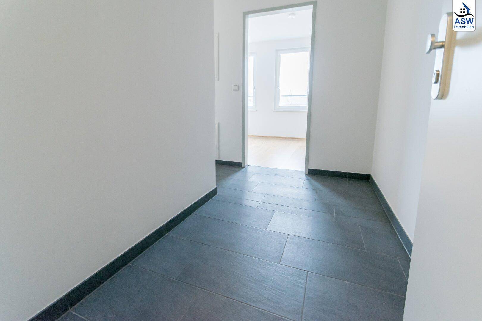 Heller Flur mit dunklen Fliesen und Zugang zu weiteren Zimmern der Wohnung.