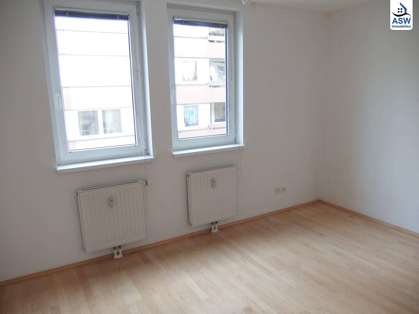 Helles Schlafzimmer mit Parkettboden und zwei großen Fenstern.