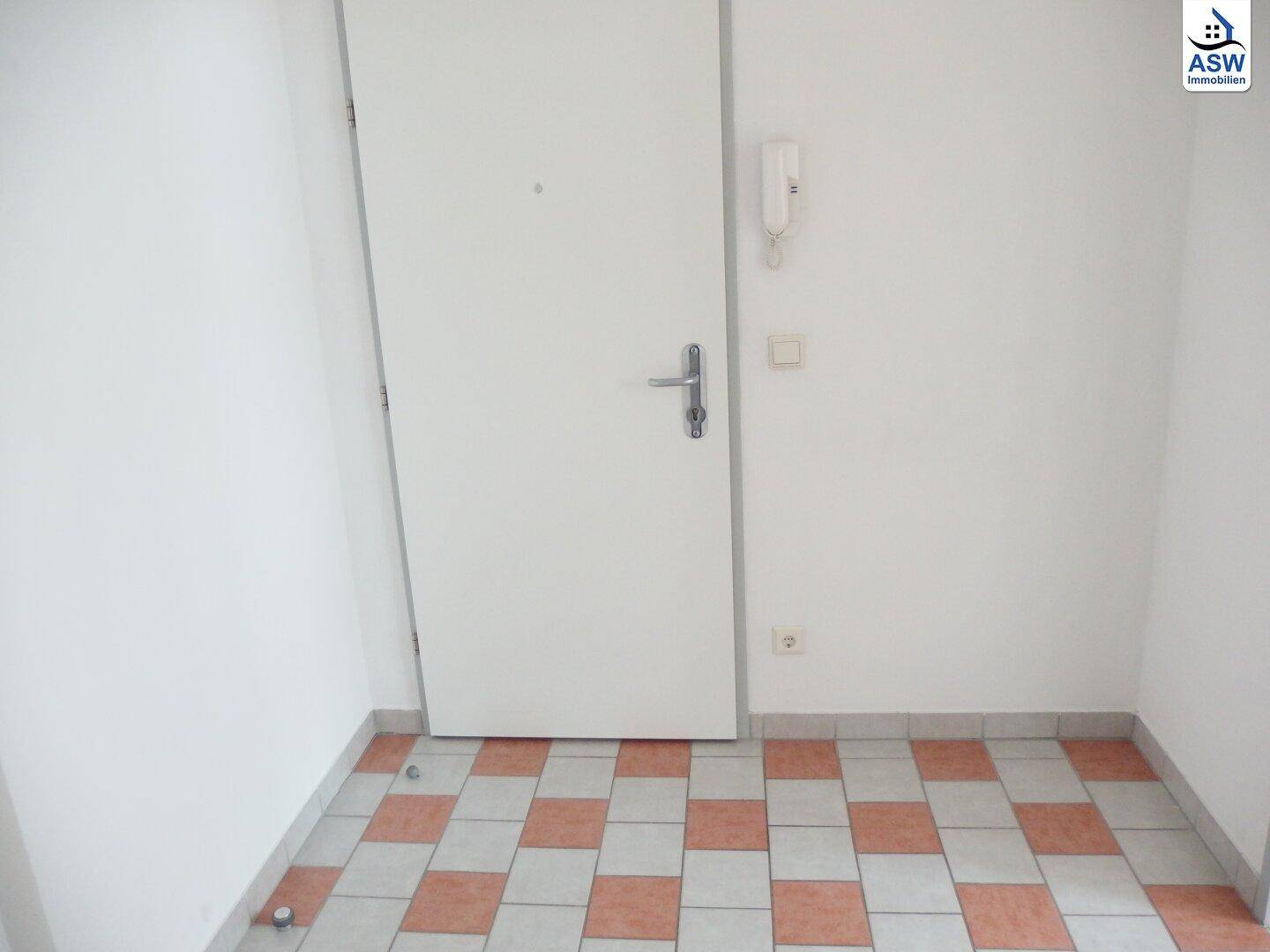Eingangsbereich mit gemustertem Fliesenboden und Gegensprechanlage.