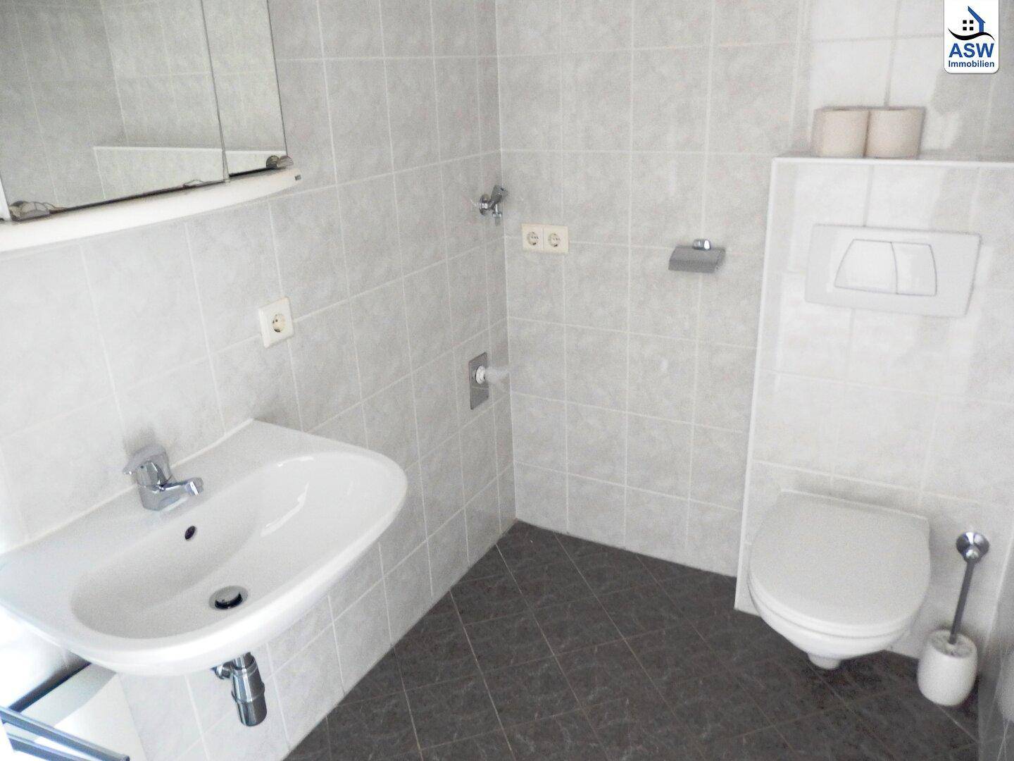 Modern gefliestes Badezimmer mit Waschbecken, Wand-WC und Spiegelschrank.