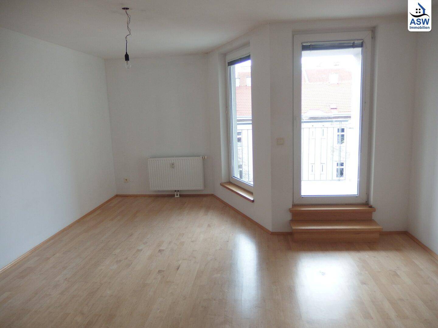 Heller Wohnbereich mit Parkettboden, Heizkörper und Zugang zu einem französischen Balkon.