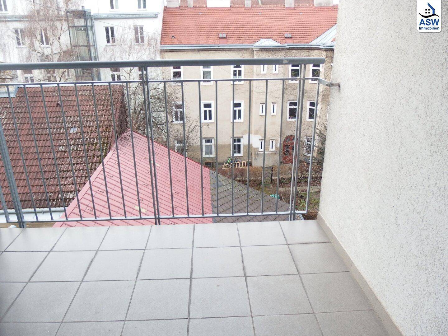 Kleiner Balkon mit Fliesenboden und Blick auf den Innenhof und umliegende Gebäude.