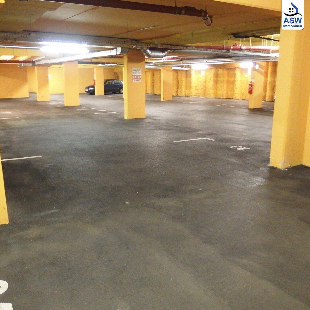 Weitläufige Tiefgarage mit gelben Stützpfeilern und dunklem Boden, ein Fahrzeug ist im Hintergrund erkennbar.