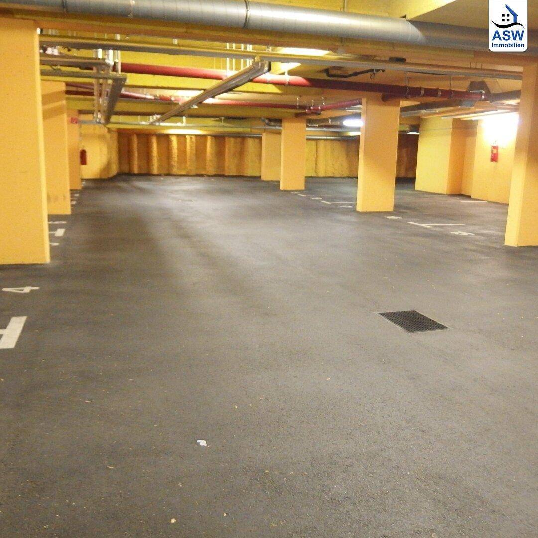 Geräumige Tiefgarage mit zahlreichen Stellplätzen, gelben Säulen und sichtbaren Installationen an der Decke.