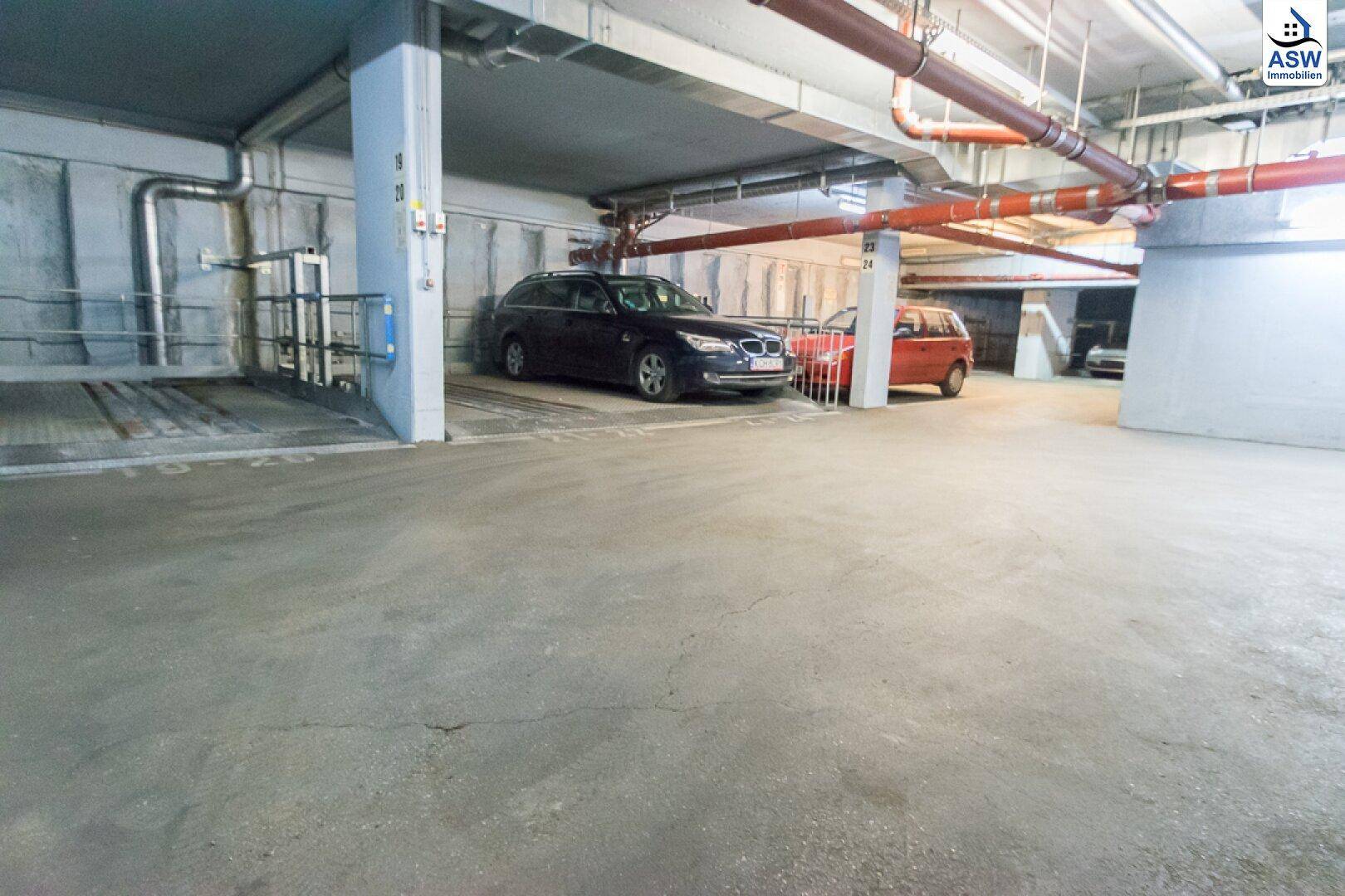 Tiefgarage mit mehreren geparkten Fahrzeugen und einem Autoaufzug im Hintergrund.