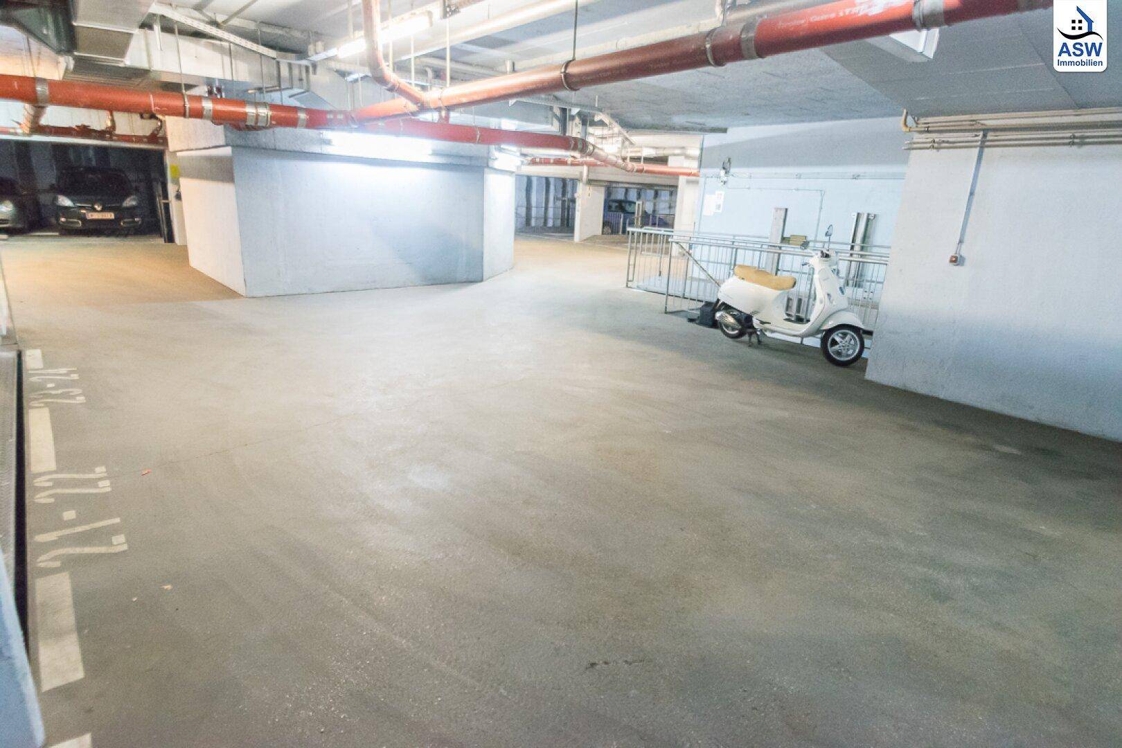 Helle Tiefgarage mit markierten Stellplätzen und einem Roller, der an der Wand lehnt.