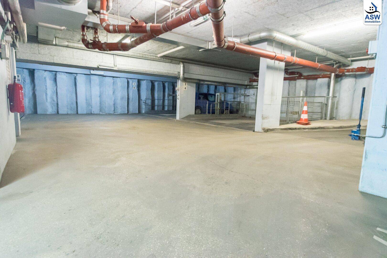 Leere Tiefgarage mit sichtbaren roten Rohren und Lüftungsanlagen an der Decke.