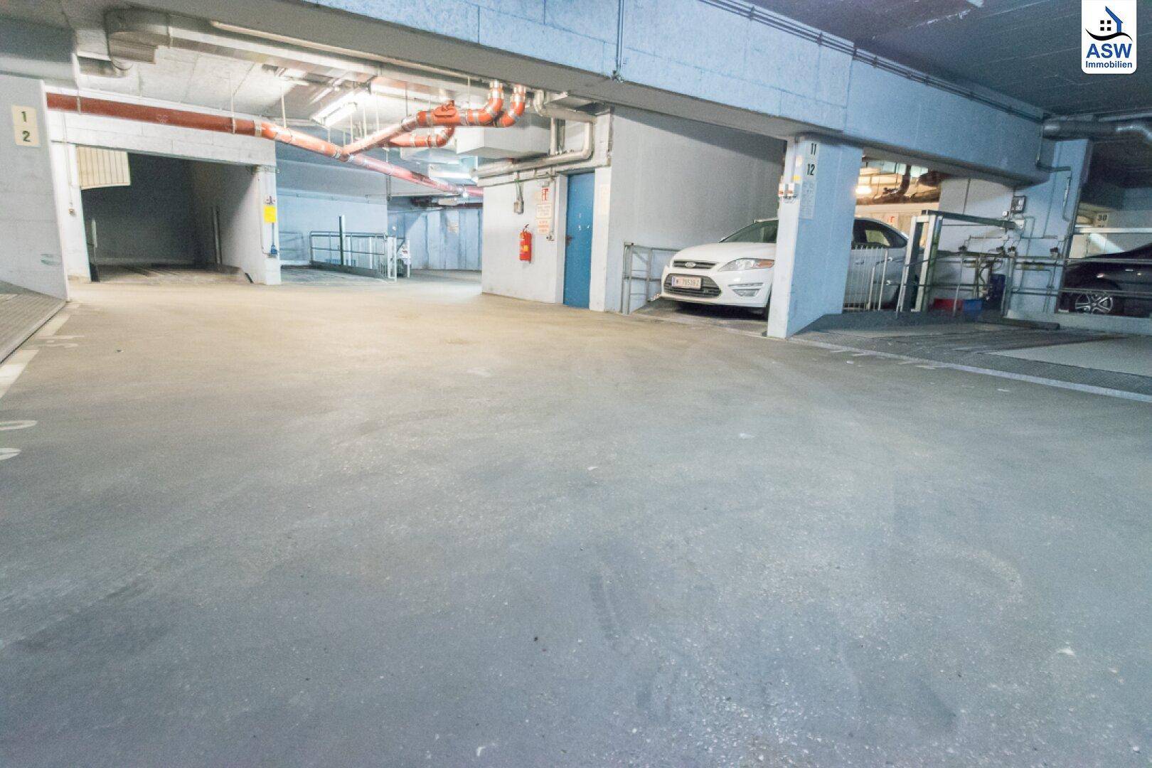 Geräumige Tiefgarage mit mehreren Stellplätzen und sichtbaren Installationen an der Decke.