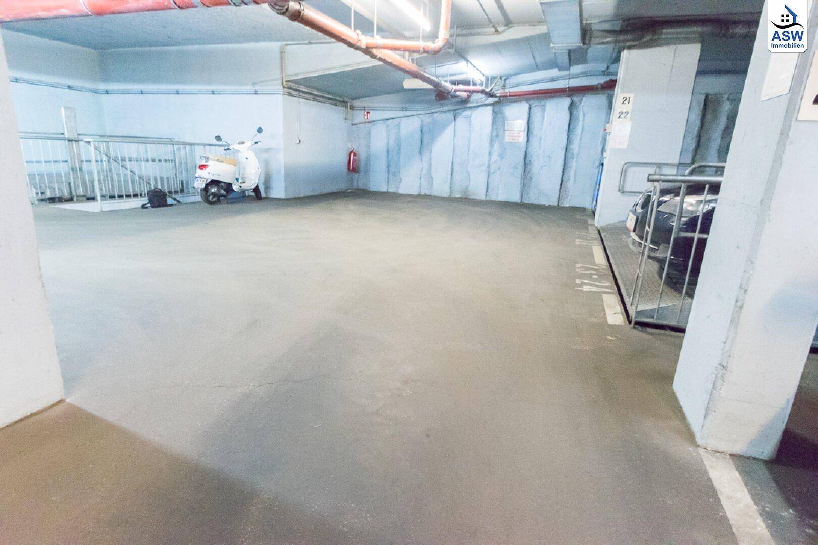 Weitläufige Tiefgarage mit einem Roller und einem geparkten Auto, gekennzeichnete Stellplätze.